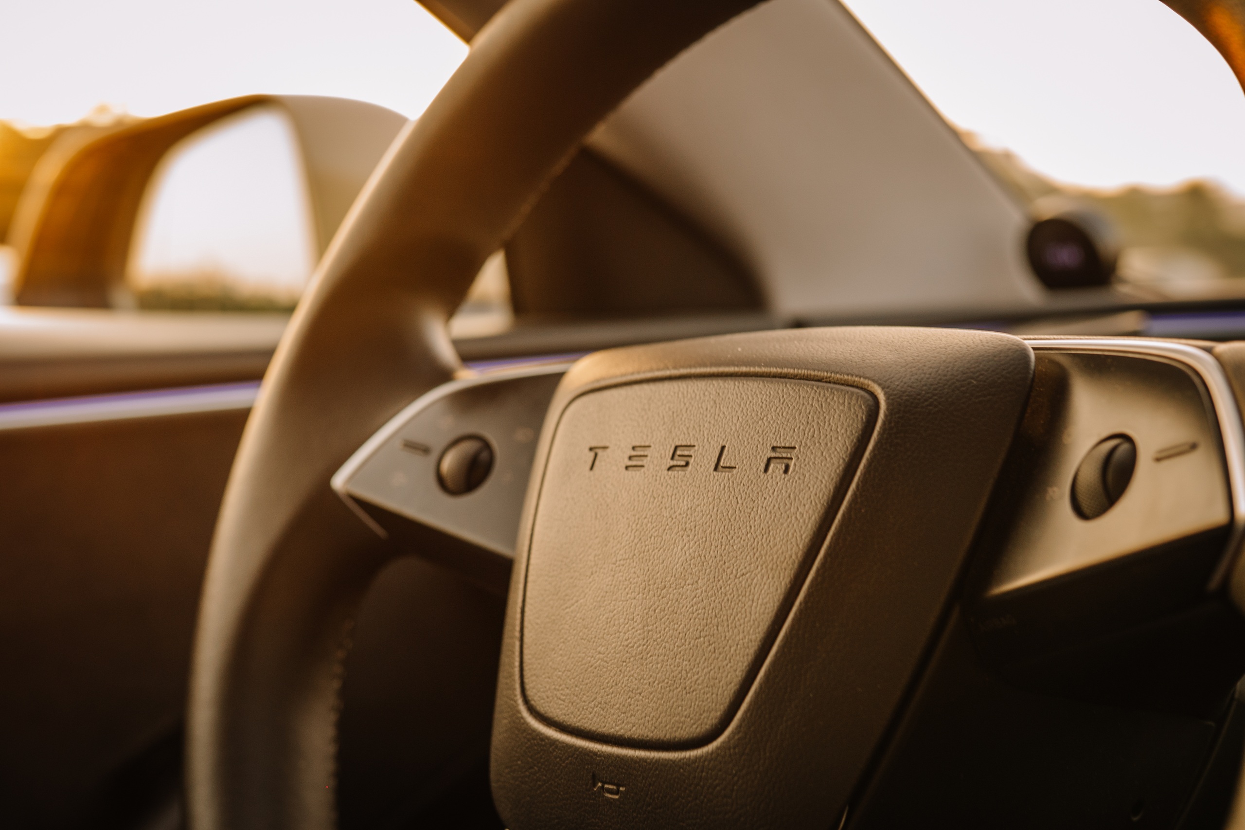 Close up view of a Tesla steering wheel with logo, interior details, and soft lighting during sunset in Dubai